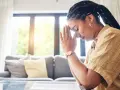A woman with braided hair and hoop earrings prays with her hands clasped, finding peace during her christian prayer times.