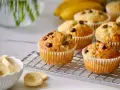 Frisch gebackene bananen muffins mit Schokostückchen auf einem Gitter, daneben eine Schüssel mit Bananenscheiben.