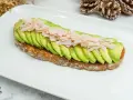 Tostada integral con aguacate en rodajas y jamón picado sobre plato blanco.
