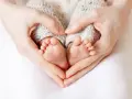 Manos formando un corazón alrededor de los pies de un bebé, evocando la protección y el complemento de maternidad con retroactividad.