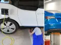 En vit elbil laddas medan en person arbetar under en blå elbil på en lyft. Service elbil är viktigt.