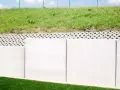 Betonowy mur oporowy z ażurową warstwą i zieloną skarpą.