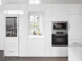 Cucina moderna bianca con elettrodomestici integrati e una porta finestra che offre una vista sul verde.
