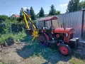 Czerwony traktor C-330 z zamontowaną żółtą koparką, gotowy do pracy w ogrodzie.