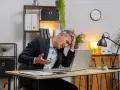 Zestresowany mężczyzna w garniturze trzyma się za głowę, patrząc na laptopa. Może właśnie stracił wadium.
