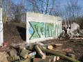 Graffiti-bemalte Überreste der Berliner Mauer, umgeben von Holzstapeln und Trümmern.