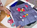 Manos revisando impresiones de arte abstracto, con vibrantes colores y patrones. El material serigrafia resalta en cada detalle.