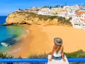 A woman in a sun hat enjoys the view of a golden beach and turquoise water in Portugal's Algarve region.