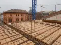 Costruzione di un solaio: mattoni forati e armature in ferro pronti per il getto di cemento. In lontananza, un edificio storico e gru edili.
