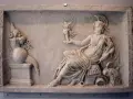 A marble relief depicting a seated figure, possibly a goddess, holding a winged victory. This scene reflects the rich tapestry of Roman paganism, with symbolic offerings and divine representation.
