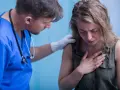 Lekarz w niebieskiej koszuli z niebieskim tłem wspiera kobietę z ręką na klatce piersiowej.