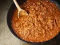 Un saporito ragù di carne in una padella, pronto per essere servito. Un cucchiaio di legno mescola la salsa ricca e densa.