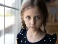 Dziewczynka z niebieskimi oczami i warkoczami, w granatowej sukience w serduszka, patrzy wprost. Jej wyraz twarzy może sugerować cechy autyzmu atypowego.