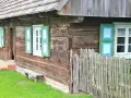 Drewniana chata z zielono-niebieskimi okiennicami, ławką i płotem. Skansen w Dziekanowicach zaprasza do podróży w czasie.