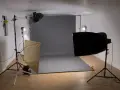 Studio fotograficzne z szarym tłem, lampami i dyfuzorem. Światło kontrowe tworzy dramatyczne cienie.