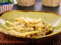 Piatto di ziti alla genovese, pasta condita con un ricco ragù di carne, servita in una ciotola verde.