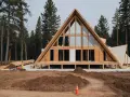 Maison en A en construction, un projet d'aide pour travaux fait soi-même. Bois, fenêtres et terrain en chantier.
