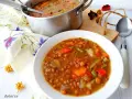 Guiso de lentejas con verduras en un cuenco blanco, junto a una olla y servilleta floral.