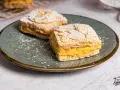 Dos porciones de pastel ruso con crema amarilla y almendras laminadas, espolvoreados con azúcar glas.