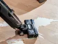A wet/dry vacuum cleaner is cleaning up a spill of white liquid and debris on a wooden floor.