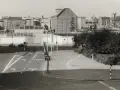 Straßenszene in Berlin der 80er Jahre mit Autos, Ampeln und einem Kran im Hintergrund.
