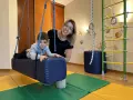 Chłopiec z ADHD u niemowlaka ćwiczy na huśtawce terapeutycznej z uśmiechniętą fizjoterapeutką.