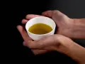 Mani che sorreggono una tazzina bianca con olio extravergine di oliva dorato. Un gesto per imparare come riconoscere olio extravergine di oliva.