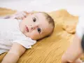 Niemowlę leży na musztardowym kocyku. Kiedy się niepokoić, gdy dziecko nie chodzi? Zwykle nie ma powodu do obaw, jeśli maluch rozwija się prawidłowo.