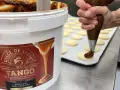 Un repostero usa una manga pastelera para decorar galletas con dulce de leche, mostrando cómo hacer dulce de leche.