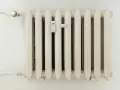 Biały grzejnik żeberkowy z termometrem i zaworem. Optymalna temperatura dla taryfy g12.