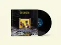 Pochette de l'album "To the Faithful Departed" de The Cranberries, avec un vinyle noir à côté. Le groupe pose dans une structure jaune au milieu d'une forêt enneigée.