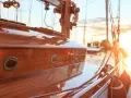 Glänzendes Holzdeck eines Segelboots, frisch lackiert. Kleine Bullaugen spiegeln die untergehende Sonne wider.
