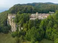 A monastery complex clings to a sheer cliff face in La Verna, Italy, surrounded by lush green forests.
