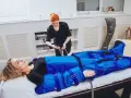 Kobieta w salonie piękności przechodzi zabieg drenażu limfatycznego. Terapeuta przygotowuje urządzenie do masażu uciskowego.