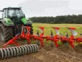 Zielony traktor z pługiem obrotowym pracuje na polu, przygotowując ziemię do siewu.
