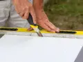 Ręce trzymają nóż, którym ciąć styropian wzdłuż żółtej poziomicy. Precyzyjne cięcie materiału izolacyjnego.