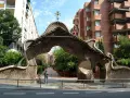 Portail organique, œuvre de Gaudí à Barcelone, avec une statue d'homme devant.