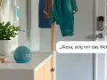 Alexa Routine erstellen: Ein blauer Echo Dot mit leuchtender Uhrzeit und eine Pflanze stehen auf einer Kommode. Eine Jacke hängt an einem Kleiderständer.