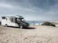Eura Mobil husbil parkerad på en sandstrand vid havet. Ett par står och tittar ut över vågorna.