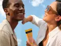 Un couple rit sous un ciel bleu, une femme appliquant une crème solaire Neutrogena. Une liste de protection contre le soleil pour une peau saine.