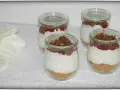 Vier leckere Desserts im Glas mit Krümelboden, cremiger Füllung, roter Fruchtsauce und knusprigem Topping.