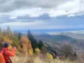 Widok na Beskid Mały jesienią. Turysta z pomarańczowym plecakiem fotografuje panoramę.