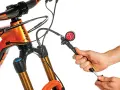 Adjusting the mtb suspension setup. A hand uses a shock pump with a gauge to set the air pressure on an orange mountain bike's front fork.