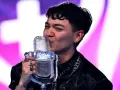 Młody artysta całuje mikrofon z logo konkursu piosenki Eurowizji, świętując zwycięstwo.
