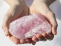 Manos sostienen una gran piedra de cuarzo rosa, una piedra para la salud y el bienestar, con su translúcida belleza.