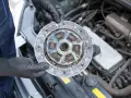Mechanik w czarnych rękawiczkach trzyma zużyte sprzęgło samochodowe na tle silnika.