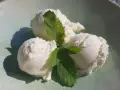 Drei Kugeln cremiges Bergamotte Eis mit frischer Minze auf einem hellgrünen Teller.