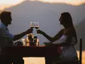 Idealne miejsce na pierwszą randkę: para wznosi toast winem przy romantycznej kolacji na tle zachodzącego słońca i gór.