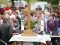 Holzkreuz mit Blumen und Kerzen vor einer Gemeinde. Ein Thema, das auch bei unterschiedlichen Konfessionen von Ehepartnern relevant ist: die Kirchensteuer.