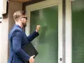Mężczyzna w garniturze puka do drzwi, niosąc teczkę. Zastanawia się, ile zabierze komornik z premii.